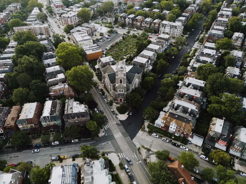 Aerial view of a Philadelphia neighborhood of rowhouses and tree-lined streets with a church at the center