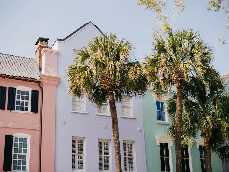 Pastel-colored historic row houses and palmetto trees on a sunny Charleston street