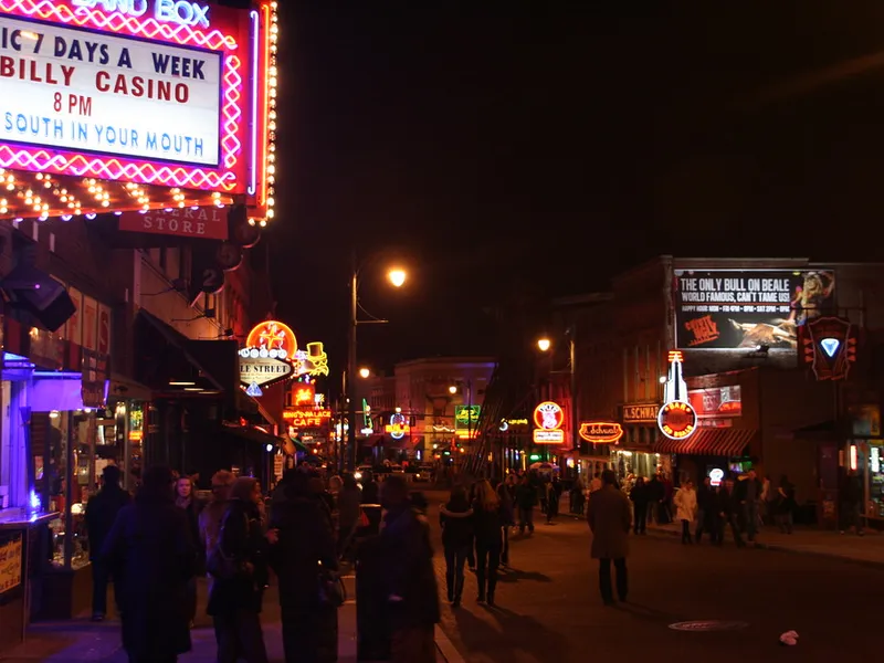 Crowds walking along Beale Street in Memphis at night beneath glowing neon signs and music venue marquees