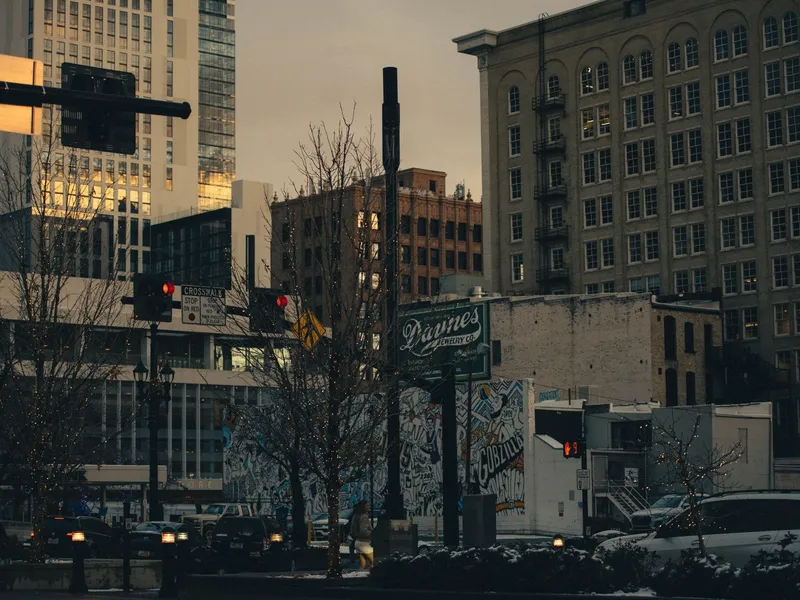 Downtown Salt Lake City street at dusk with historic brick buildings, a mural, traffic and a pedestrian crossing