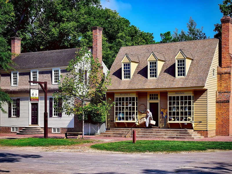 Colonial shop and houses on a quiet street in Williamsburg, Virginia, with a costumed woman leaving the store