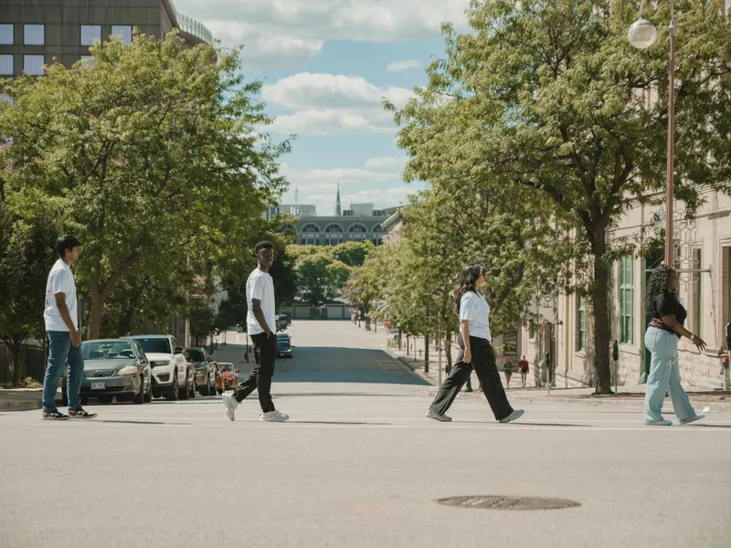 Four young people walking across a tree-lined city street in Milwaukee, Wisconsin on a sunny day