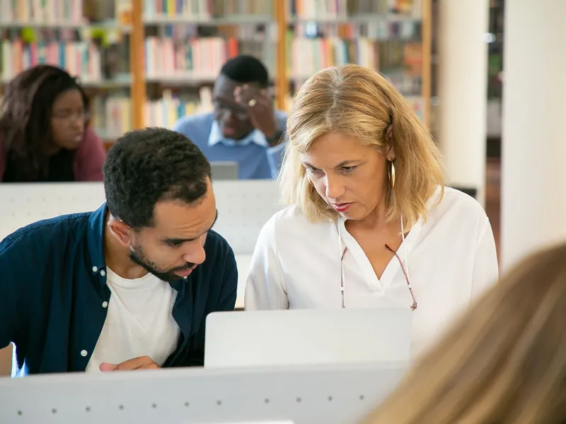 Student explaining his study plan to a professor in a university library