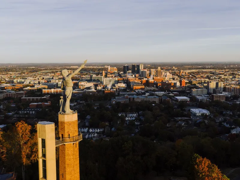 Vulcan statue on its stone tower overlooking the Birmingham, Alabama skyline and surrounding autumn trees at sunset
