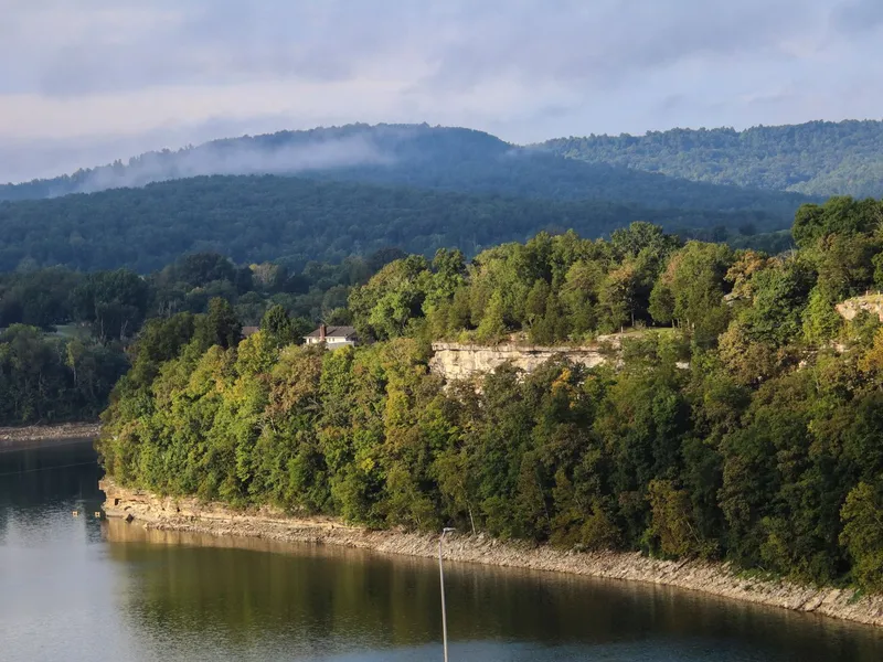 Forested limestone bluffs and rolling green hills rising above a calm river in the Ozarks