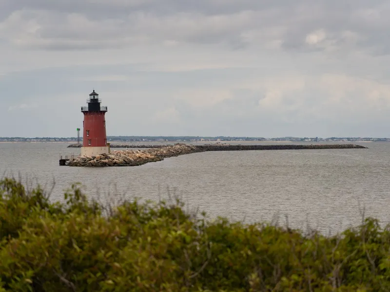 Red Breakwater Lighthouse on a stone jetty in Delaware Bay off Lewes under a cloudy sky