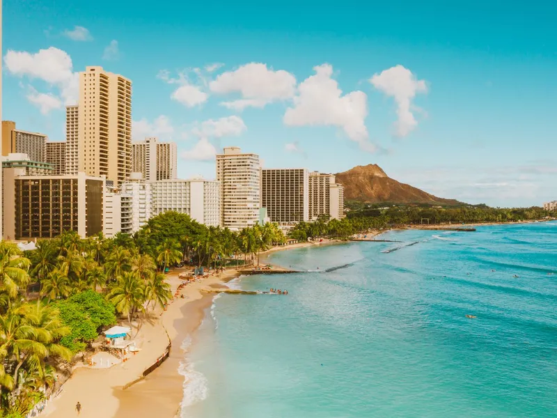 Waikiki Beach with high-rise hotels, palm trees and Diamond Head under a bright blue sky