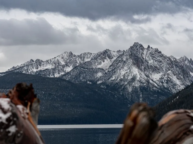Snow-capped Sawtooth Mountains rising above a calm lake in Idaho under heavy clouds