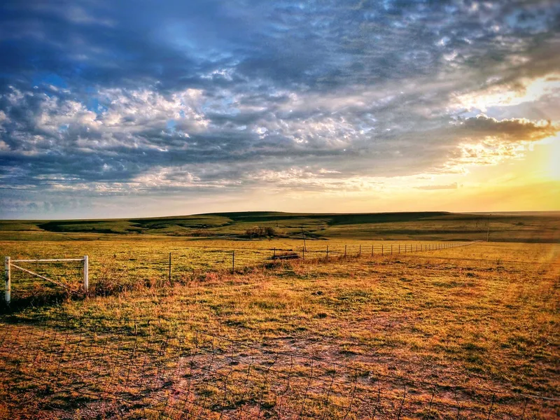 Rolling Kansas prairie pasture with a fence line under a dramatic sunrise sky