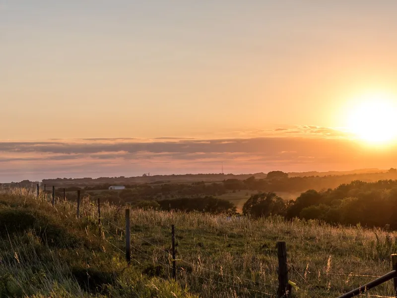 Sunrise over rural Nebraska fields and trees with a fence in the foreground