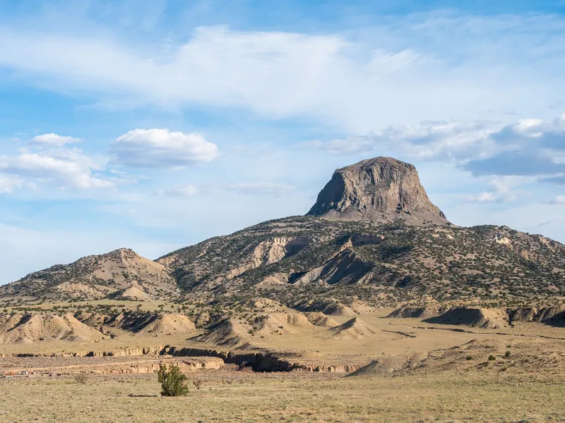 Cabezon Peak rising above desert badlands and sagebrush grassland in New Mexico under a bright sky