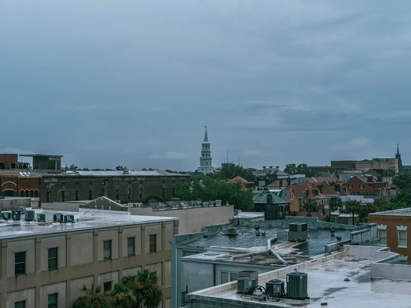 Rooftops of historic Charleston, South Carolina, with a white church steeple rising under a stormy sky