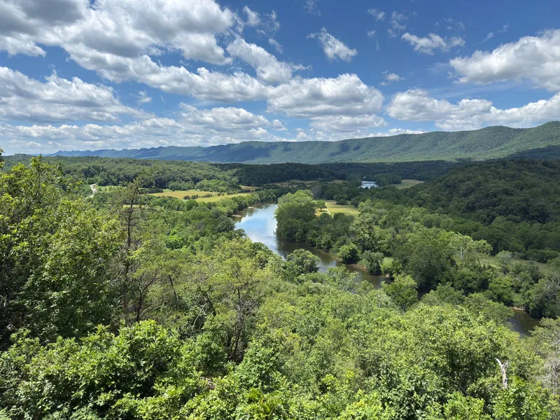 Winding Shenandoah River below forested ridges of the Blue Ridge Mountains under a blue sky with clouds