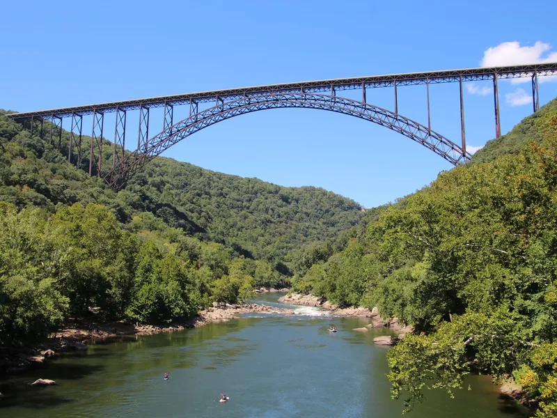New River Gorge Bridge arching over a river valley with kayakers and green forested hills
